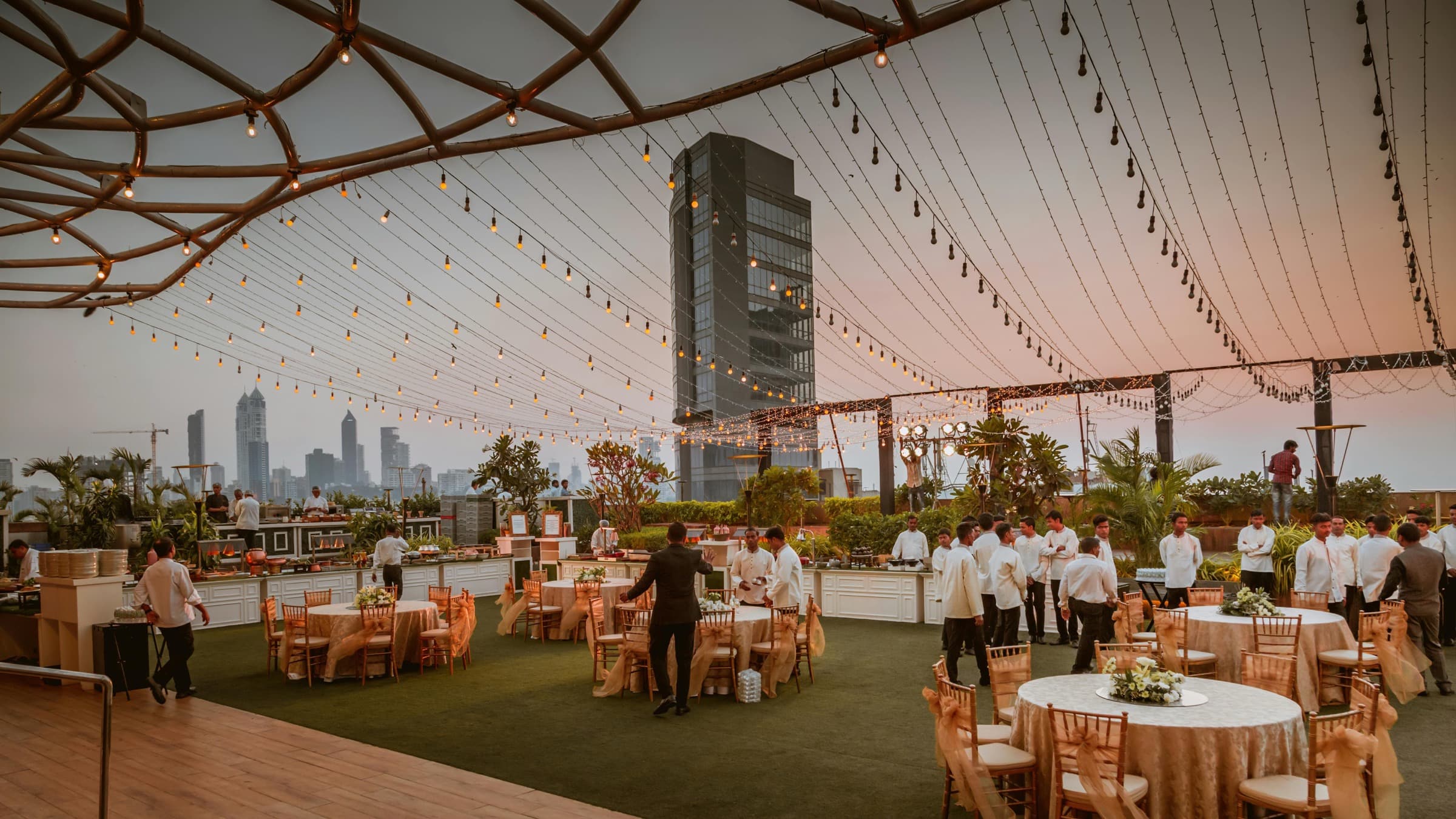 Rooftop reception set with round tables under string lights at dusk